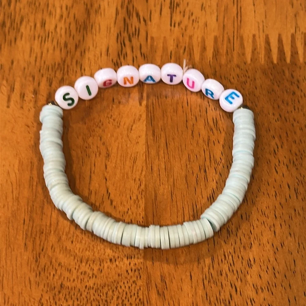 Kids shell bracelet with the word “signature”. Light teal shells.